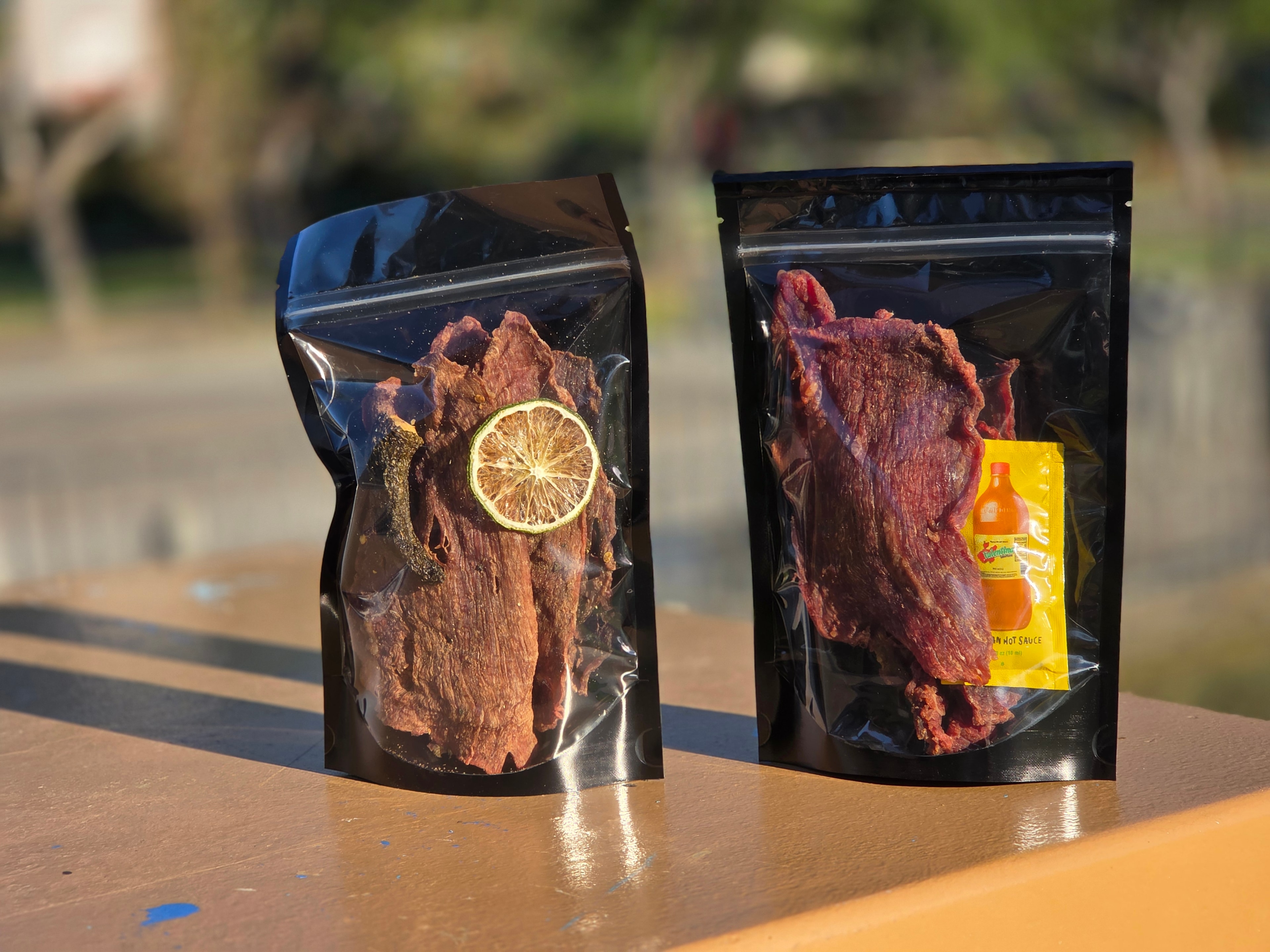 Two bags of Knuckle Dragger carne seca — garlic lime and chipotle lime with Valentina packet